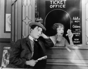 1924: American comedian Buster Keaton (1895-1966) standing outside the box office clutching his dollar bill while Ruth Holly applies her make-up in the film 'Sherlock Junior'.